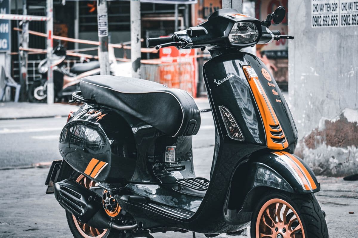 Vespa Sprint negra con detalles naranjas, estacionada en la vereda