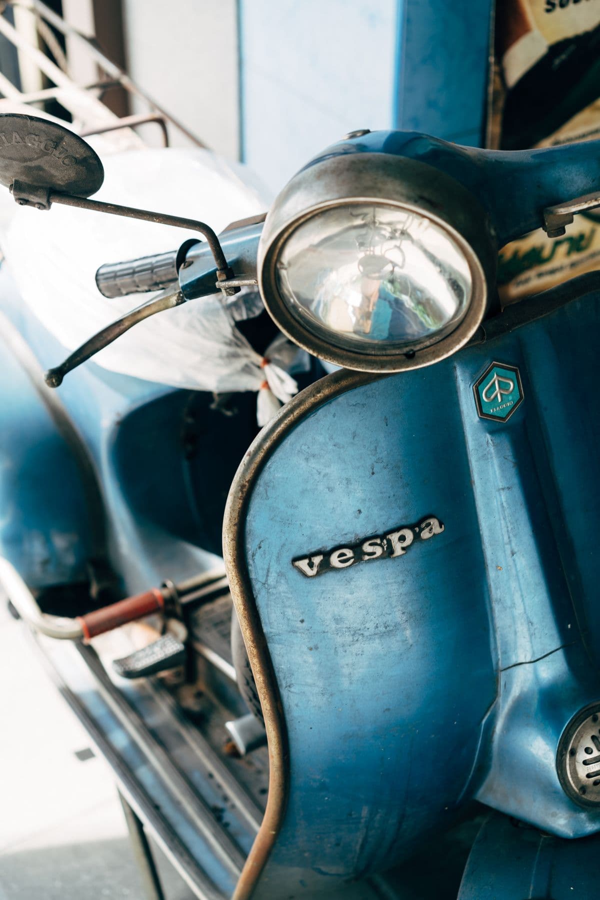 Vespa clásica azul con la pintura gastada por los años y el escudo Piaggio