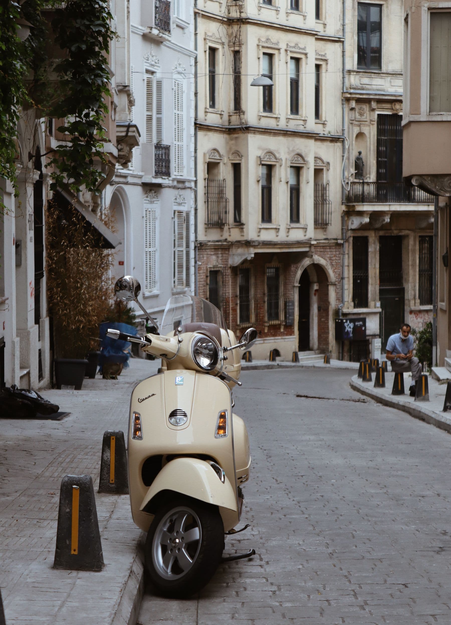 Vespa GTS color crema estacionada en una calle empedrada de casas ocres